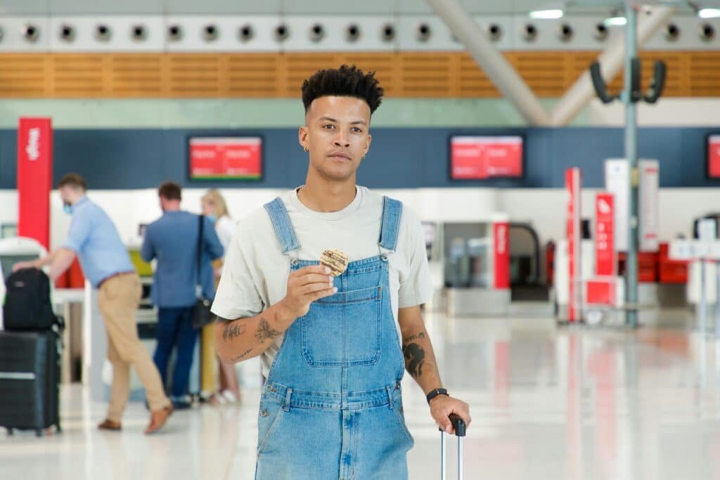 Young man in denim jumper with cookie at airport terminal, ready to travel.