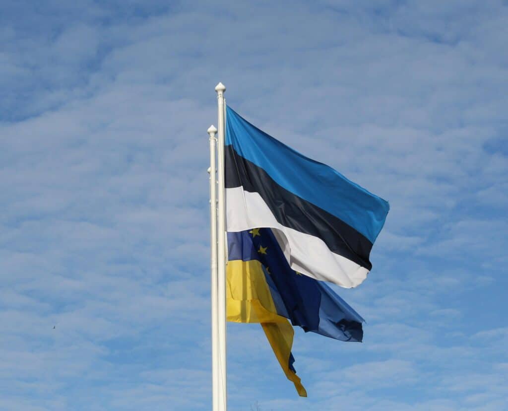 National flags of Estonia, Ukraine, and the EU waving against a clear blue sky. Symbolic and vibrant.